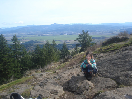 a boy hiking up a gentle hill, looking down at a boulder